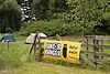 Banner mit Aufschrift Juniorrangercamp und dem Logo der Naturwacht an einem Zaun angehängt, im Hintergrund zwei Zelte auf einer Wiese